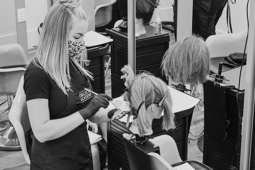 Black and white image of a woman sitting with a stylist behind her.