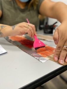 Woman coloring a strip of fake hair for practice.